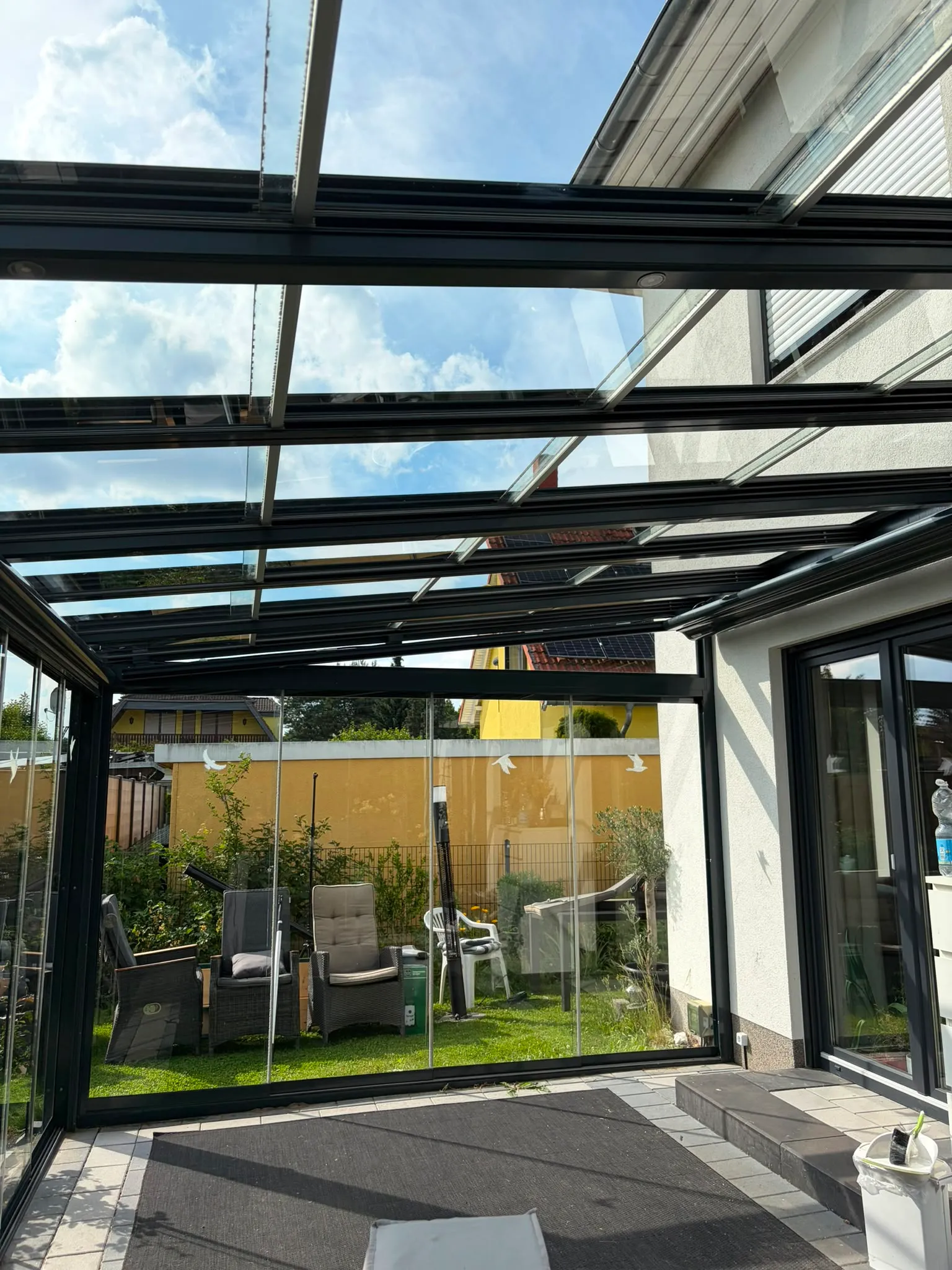 Streifenfrei gereinigtes anthrazitfarbenes Glas-Terrassendach mit Blick in den Garten
