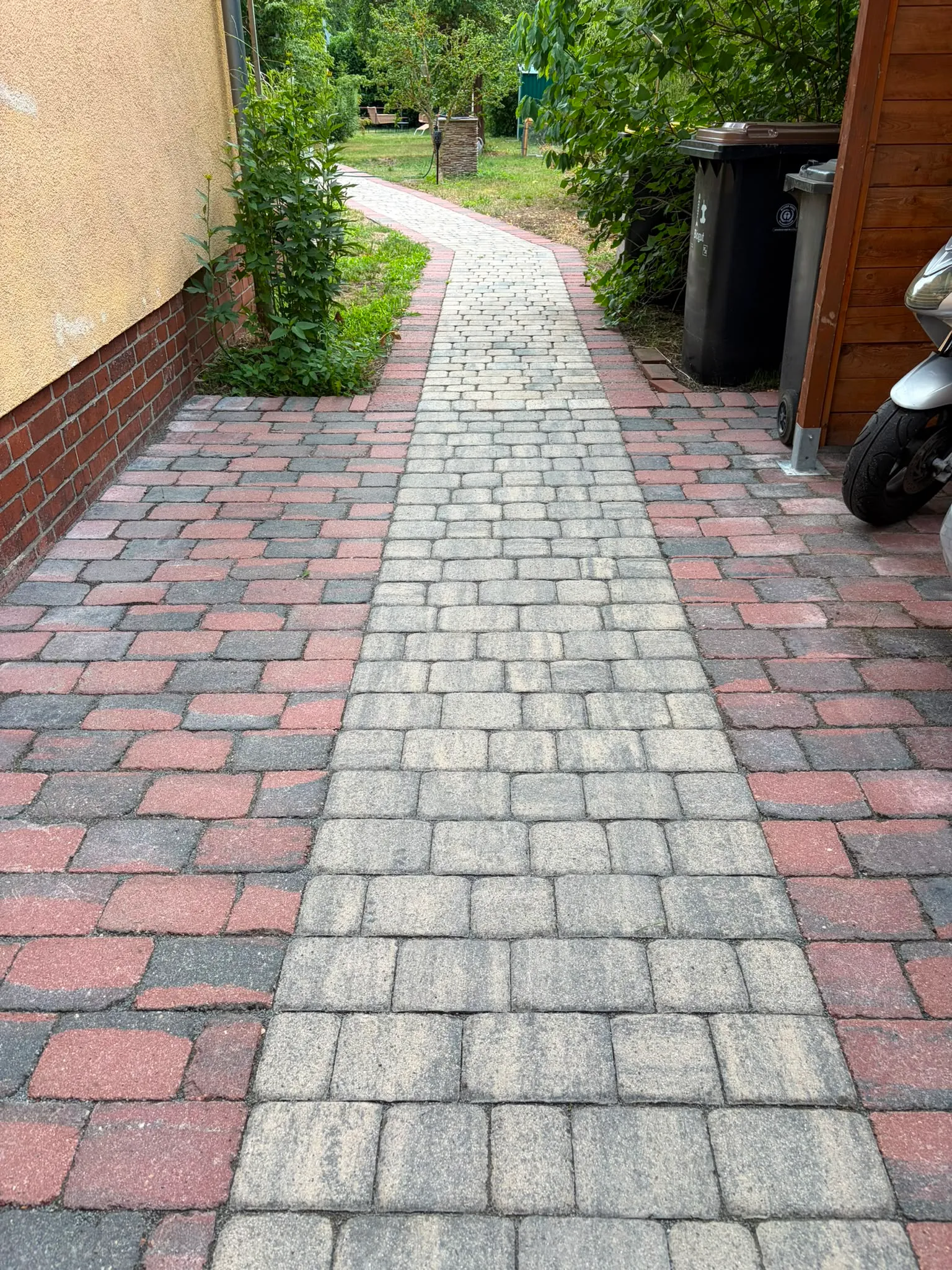 Gepflasterter Weg mit deutlich sichtbarem, frisch hochdruckgereinigtem hellen Streifen